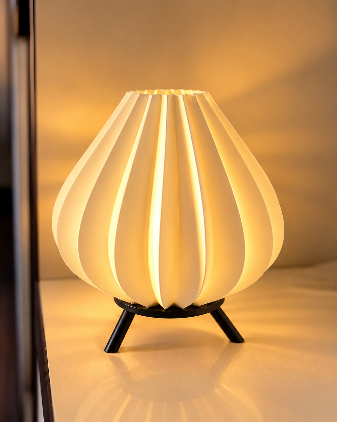 Glowing table lamp with a petal-like fluted shade and black tripod base.